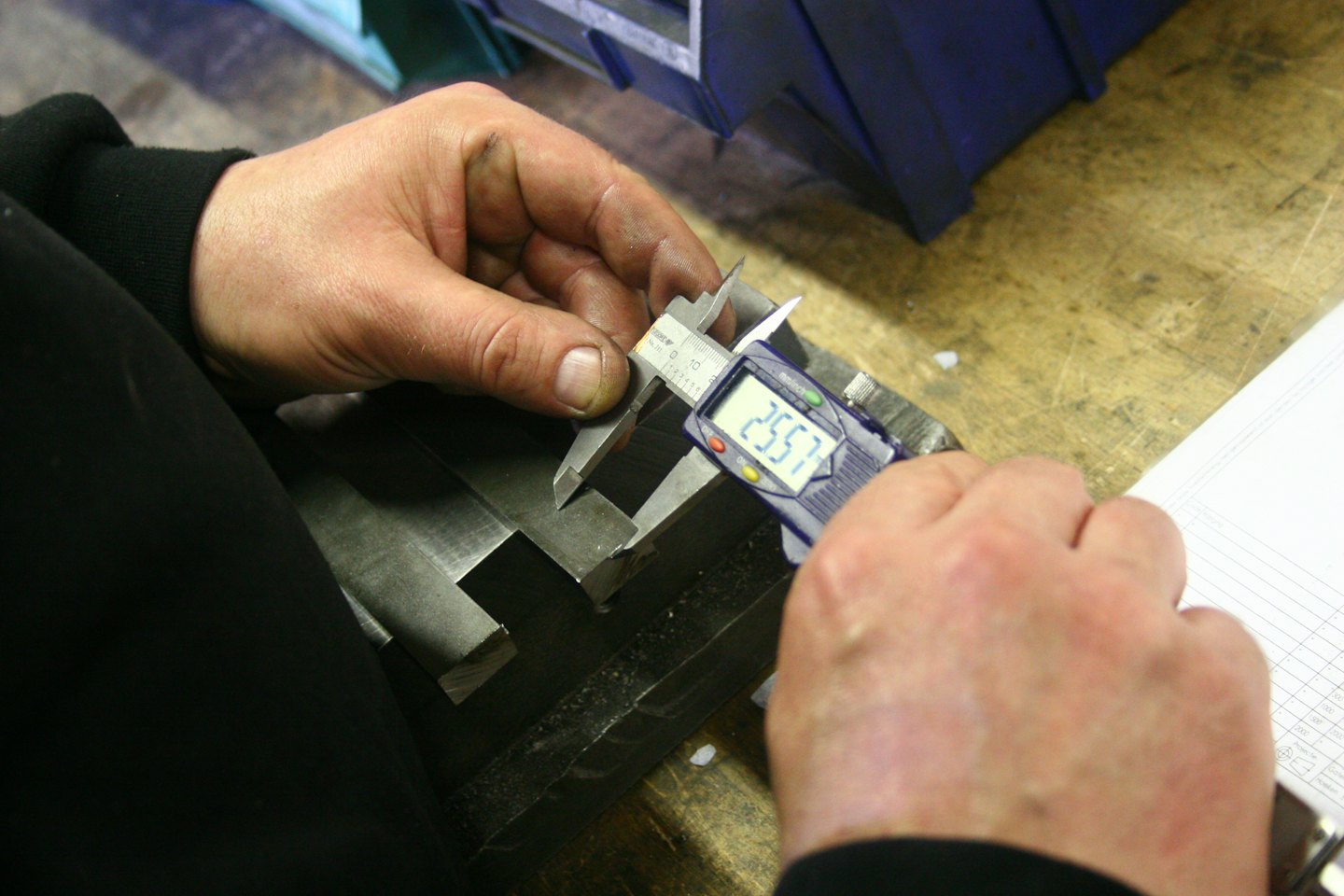 Hände benutzen ein digitales Messschieber, um ein Metallteil zu messen.