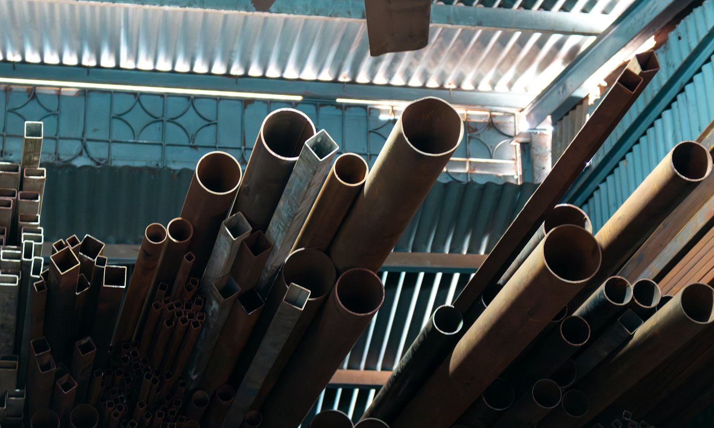 Ein Stapel rostiger Metallrohre in einer Lagerhalle.